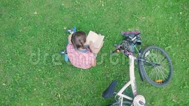 顶景可爱的女孩在公园里坐在草地上读一本好书