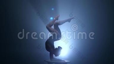体操运动员在演播室的桌子上<strong>表演魔术</strong>。 烟雾背景。 慢动作。 剪影