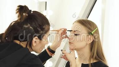 女人在婚礼前为年轻女人化妆眉毛和脸。 女人脸上画着眉毛