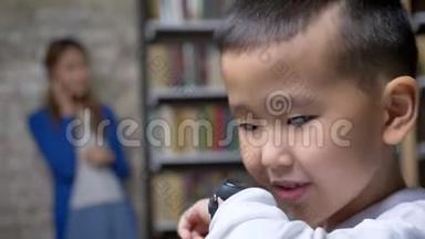 小亚洲男孩通过智能手表、书架和砖墙背景与母亲交谈
