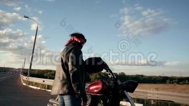 一个穿着皮夹克和手套的老妇人骑自行车来到他的摩托车前，转身<strong>面对</strong>相机。 <strong>微笑</strong>的女人可以