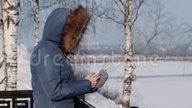 穿着蓝羽绒服的女人在冬天公园的手机里写短信。 侧视图