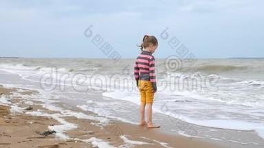 可爱的<strong>女孩</strong>看着大海中的波浪站在<strong>水边</strong>。 海上风暴，强风巨浪