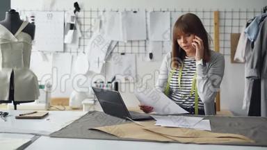 服装设计师正在讨论手机上的服装草图，并在笔记本电脑中输入信息。 忙碌的一天