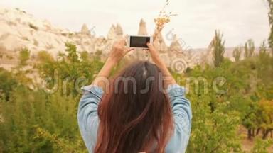 在<strong>土耳其</strong>卡帕多西亚，年轻的混合种族旅<strong>游</strong>女孩用手机拍摄美丽的山岩照片。 4K慢动作。