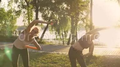 两名年轻女子在公园做有氧运动，减肥，健身模式锻炼，日落和自然背景