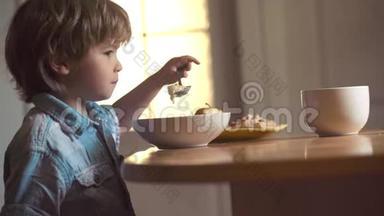 快乐的小男孩勺子吃自己。 小男孩坐在桌子旁吃牛奶零食。 宝宝在厨房吃食物