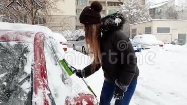 4k视频美丽微笑的年轻女子用伸缩刷子从雪中清洁汽车