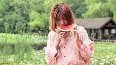 夏天的女人吃西瓜片。 微笑着在公园里吃西瓜的中国女孩。 假日生活方式。 夏季概念。