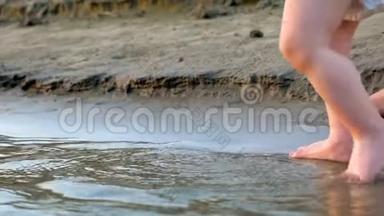 妈妈`他的手牵着孩子在海滩上。 孩子的脚上水。 慢动作。 快关门。