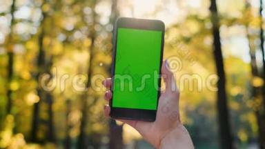 女孩显示手机绿色屏幕户外，城市环境。 女士手拿智能手机与色度键。 背面
