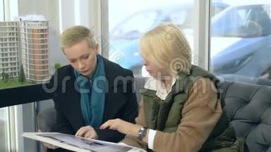 两个女人正在说话，坐在售楼处的背景上布置着大楼