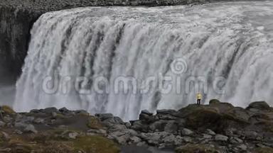一个年轻的女人欣赏一个强大的狂暴瀑布，沿着岩石边缘重重地落下。 一条晶莹清澈的冰川水流