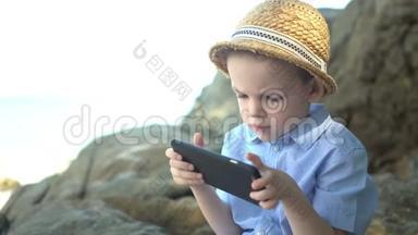 可爱的男孩坐在石头上，使用智能<strong>手机</strong>，在海边<strong>看手机</strong>应用程序