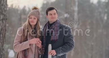 一对相爱的夫妇在冬天的森林里喝热水瓶里的茶。 穿外套的时髦男女