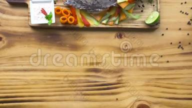 烧烤餐厅用蔬菜装饰的烤鱼。 木制桌子上有蔬菜的食物组成鱼烧烤