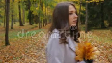 美丽的年轻女子在秋天的公园里等待着一个人，她用枫叶花束微笑着对一个人说