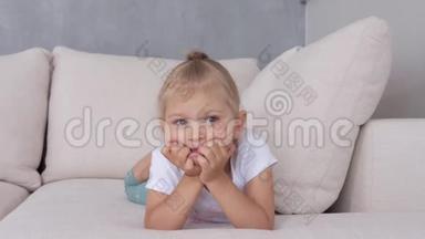 一个小女孩躺在柔软的沙发上看着电视<strong>屏</strong>幕。