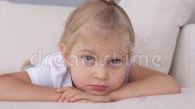 一个小女孩躺在柔软的沙发上看着电视<strong>屏</strong>幕。