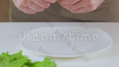 一个人在做素食午餐的时候，把绿<strong>生菜叶</strong>铺在白色盘子上。