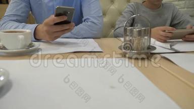 一个孩子和一个男人正在桌子上玩手机，在咖啡馆里等<strong>待订单</strong>。 特写镜头，4k