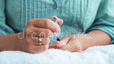 在家修指甲时，女人在指甲上涂指甲油。 女人把指甲擦得紧紧的。 家庭修指甲及