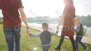 幸福的年轻家庭有两个儿子在<strong>河边</strong>的<strong>公园</strong>散步和休息。 家庭和关系概念