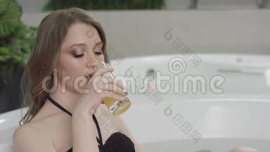 漂亮的金发女孩，穿着黑色泳衣，<strong>蓝</strong>眼睛，一边在按摩浴缸里放松，一边喝橙汁