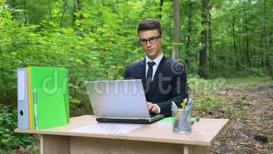 穿西装的严肃商人，在森林清新的空气里的办公桌上用笔记本电脑工作