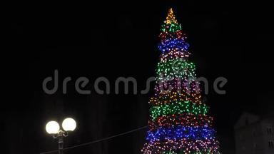 城市广场上的高圣诞树，在夜空中装饰着花环和五颜六色的气球。 小小的雪