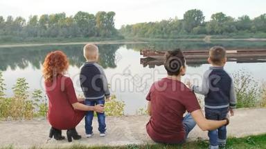 幸福的年轻家庭有两个儿子在河边的公园散步和休息。 家庭和关系概念