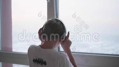 那个人站在窗户附近，通过耳机听音乐。 阳光`透过窗户照射进来