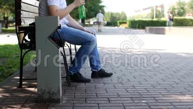 市中心的一个人坐在长凳上，把水抽干，把一个塑料瓶子扔过垃圾桶，扔垃圾