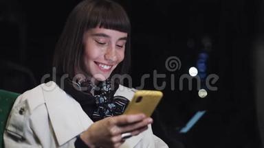 迷人的微笑年轻女子在公共交通工具使用手机。 她在发短信，检查邮件，聊天或