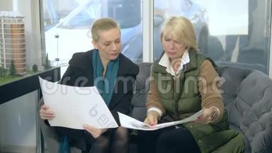 两个女人正在说话，坐在售楼处的背景上布置着大楼