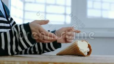 男孩`他的手从厨房的桌子上<strong>拿着</strong>一个<strong>喇叭</strong>吃冰淇淋。 穿条纹夹克的面目全非的男孩。