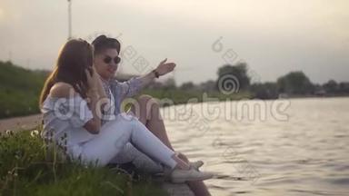 特拉迪夫妇在河边聊天。 假期，假期，爱和人的概念-快乐的青少年夫妇坐在维斯拉河边