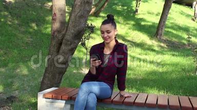 年轻漂亮的女孩穿着格子衬衫，微笑着浏览智能手机上的社交网络磁带。