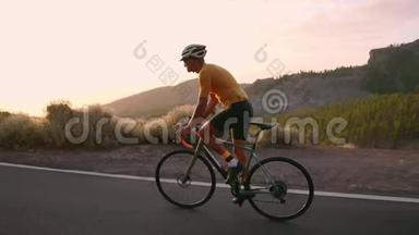 <strong>一</strong>个戴着头盔和运动装备的专业骑自行车的人<strong>在</strong>日落时缓慢地骑<strong>在</strong>山区公<strong>路上</strong>。 Stadicam
