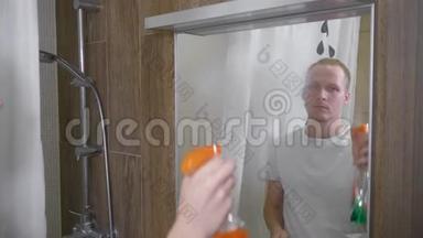 一个人打扫浴室里的镜子。 一个年轻人用纸巾清洁浴室镜子。 一个人洒在