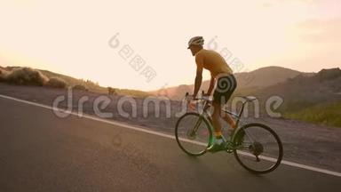 一个戴着头盔和运动装备的专业骑自行车的人在日落时缓慢地骑在山区公路上。 Stadicam