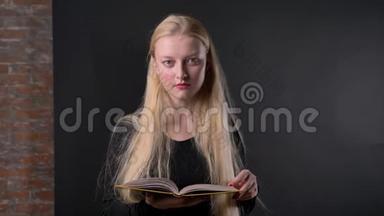 年轻漂亮的金发女孩，涂着粉红色口红，<strong>正在看书</strong>，看着相机，微笑着，灰色的背景