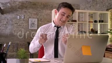 年轻的商人在办公室里拿着笔记本电脑工作，因为生意的胜利而高兴，手握拳，做手势