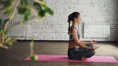 侧面观看<strong>瑜伽学生</strong>放松和呼吸，同时坐在莲花的位置上明亮的垫子。 有魅力的女人