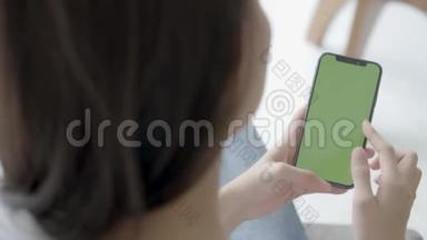 亚洲女人手牵着手，看着用绿色屏幕的智能手机在沙发上自己定制内容