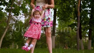 妈妈正和一个快乐的笑女儿在空中握手。 家长在夏日公园的草地上玩耍