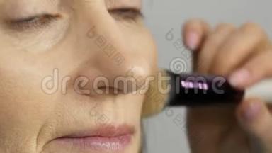 化妆师用高光<strong>遮瑕</strong>膏给蓝眼睛的中年妇女化妆。 年龄化妆。 特写肖像