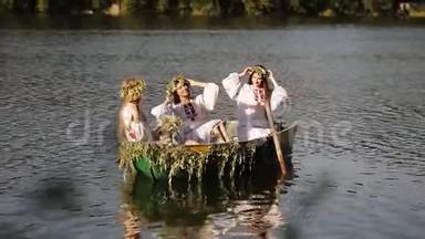 三个女孩穿着斯拉夫民族服装坐着一艘船漂浮在河上。 戴花环的女孩。 斯拉夫女孩