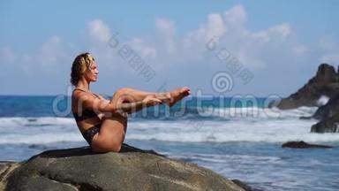一个穿比基尼的年轻女孩坐在石头上，<strong>交替</strong>地举起腹部肌肉做运动
