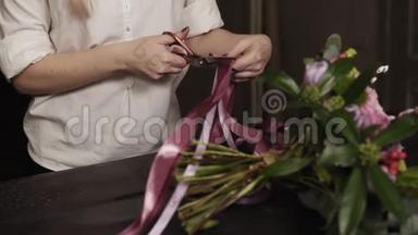 一个穿着白色衬衫的女孩剪下粉红色的长丝带和紫色的宽丝带，装饰一束鲜花